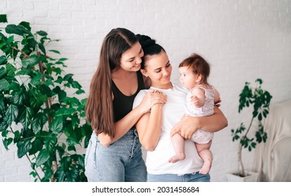 Two beautiful young women in casual clothes hug and look at their little child in the apartment. the concept of lgbt people. lesbian  marriage and adoption, homosexuals-a lesbian couple.