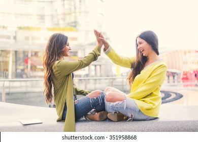 Two Beautiful Young Women Giving High Five - Pretty Girls Sitting On A Bench Outdoors And Having Fun - Best Girlfriends Making A Promise