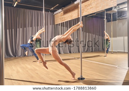 Two beautiful young women in gymnastics clothes showing acrobatic performance in pole dance studio