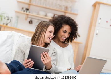 Two Beautiful Young Women Relaxing On The Living Room Floor Looking At A Laptop Computer And Laughing At Something On The Screen