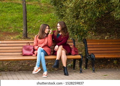 Two beautiful young women resting on a bench in the autumn park