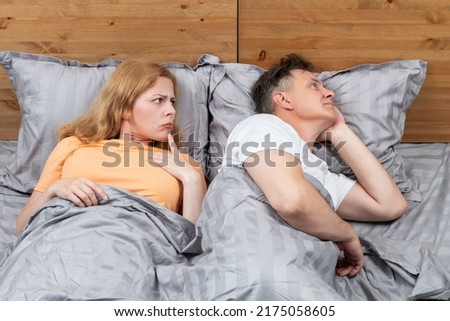 Two in bed, a woman looks with suspicion at a man who has turned away in the other direction. Relationship concept