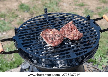 two beef steaks searing on a black charcoal barbecue grill,