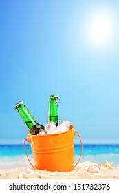 Two Beer Bottles In A Bucket Of Ice In The Sand On A Beach