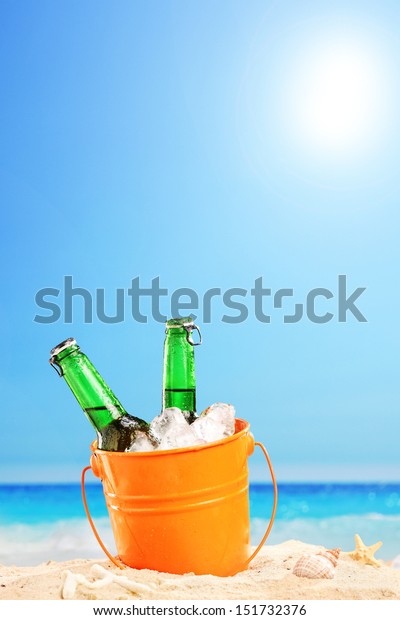 Two beer bottles in a bucket of ice in the sand on\
a beach
