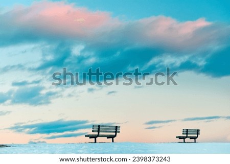 Two benches on a snow-covered glade against the backdrop of a gentle sunset sky. Minimalism.
