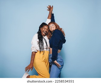 Two best friends dancing and having a good time together in a studio. Happy young women enjoying themselves while standing against a blue background. Female friends making cheerful memories. - Powered by Shutterstock