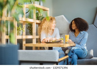 Two best friends enjoying nice conversation during lunch in modern cafe interior. African woman dining at restaurant together with white curly female. People, leisure, communication and friendship. - Powered by Shutterstock