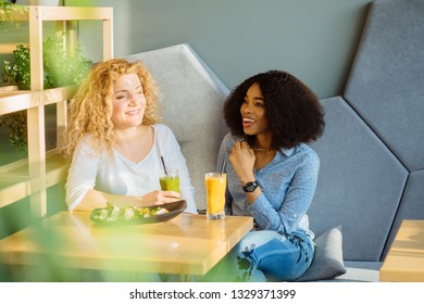 Two best friends enjoying nice conversation during lunch in modern cafe interior. African woman dining at restaurant together with white curly female. People, leisure, communication and friendship. - Powered by Shutterstock