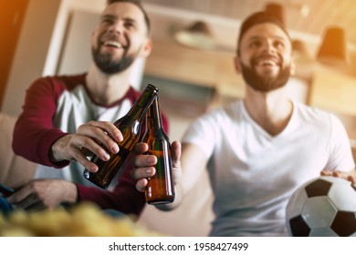 Two Best Friends And Fans Of Football Watching Some Sport Match On The TV And Drinking Beers And Eating Snacks While Cheering For The Team On The Couch