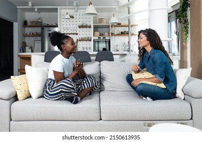 Two Best Friends Hanging Out At Home Together And Having Fun While Sitting On The Couch In Cozy Modern Apartment. Two Women Gossip About The Men They Met Last Night Out At The Party In The Club.