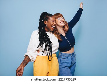 Two best friends laughing and having fun while embracing each other in a studio. Happy young women enjoying themselves while standing against a blue background. Friends making cheerful memories. - Powered by Shutterstock