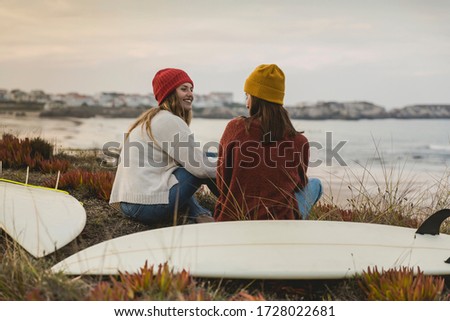 Two best friends sitting near the coastline with her surfboards while looking to the ocean