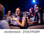 Two best friends are watching a movie in cinema and they are eating popcorn.