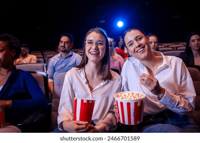 Two best friends are watching a movie in cinema and they are eating popcorn. - Powered by Shutterstock