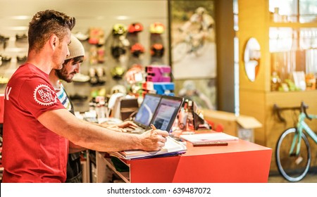 Two bicycle repairer colleagues working in bike garage cafe -  Racing superbikes and mountainbikes seller using computer in workshop  - Retail selling concept - Focus on right man hand - Warm filter - Powered by Shutterstock
