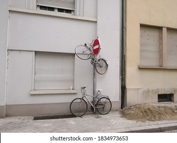 Two Bicycles Attached To The Post With Traffic Sign: One Bicycle On The Ground And The Second One In The Air, Attached On The Top The Post In The Street. Bicycle Fixed On The Pillar. Urban Joke Or Gag