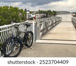 Two bicycles parked together by entrance ramp at a riverside marina in Punta Gorda, Florida, with a view of the northbound US 41 traffic bridge across Peace River, on a cloudy day in southwest Florida