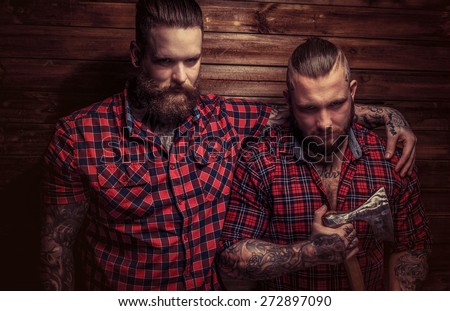 Two big brutal males with beards and tattooes and one of them holds axe