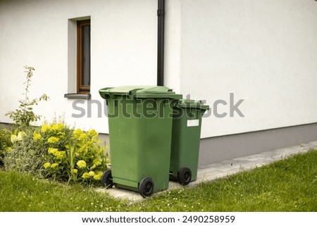 Two Big empty green plastic trash garbage bin in front of the modern house. Plastic pollution problem.