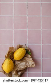 Two Big Lemons With A Green Leaf In A Torn Brown Shopping Craft Paper Bag On A Pink Tile Kitchen Countertop Background. Minimal Flat Lay With Copy Space. Summer Background.