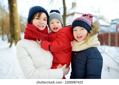 Two Big Sisters And Their Toddler Brother Having Fun Outdoors. Two Young Girls Holding Their Sibling Boy On Winter Day. Kids During Winter Break. Children Exploring Nature Together.