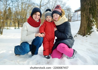 Two Big Sisters And Their Toddler Brother Having Fun Outdoors. Two Young Girls Holding Their Sibling Boy On Winter Day. Kids During Winter Break. Children Exploring Nature Together.