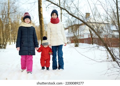 Two Big Sisters And Their Toddler Brother Having Fun Outdoors. Two Young Girls Holding Their Sibling Boy On Winter Day. Kids During Winter Break. Children Exploring Nature Together.