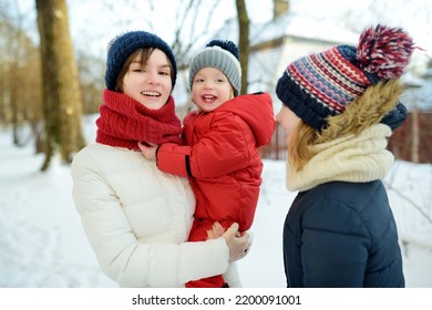 Two Big Sisters And Their Toddler Brother Having Fun Outdoors. Two Young Girls Holding Their Sibling Boy On Winter Day. Kids During Winter Break. Children Exploring Nature Together.