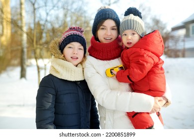 Two Big Sisters And Their Toddler Brother Having Fun Outdoors. Two Young Girls Holding Their Sibling Boy On Winter Day. Kids During Winter Break. Children Exploring Nature Together.