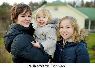 Two Big Sisters And Their Toddler Brother Having Fun Outdoors. Two Young Girls Holding Their Sibling Boy On Winter Day. Kids During Winter Break. Children Exploring Nature Together.