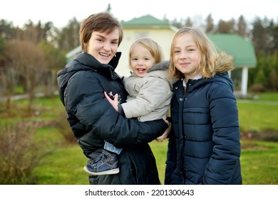 Two Big Sisters And Their Toddler Brother Having Fun Outdoors. Two Young Girls Holding Their Sibling Boy On Winter Day. Kids During Winter Break. Children Exploring Nature Together.