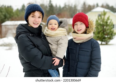 Two Big Sisters And Their Toddler Brother Having Fun Outdoors. Two Young Girls Holding Their Sibling Boy On Winter Day. Kids During Winter Break. Children Exploring Nature Together.