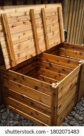 Two bin organic composter made of cedar wood with open lid for grass clippings beside fence on river rocks