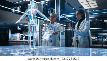 Two Bioengineers Working With Computer-Powered VFX Hologram Of Human Body And Organs In Futuristic Lab. Man And Woman Researching Blood Flow, Developing Innovative Healthcare Solutions.