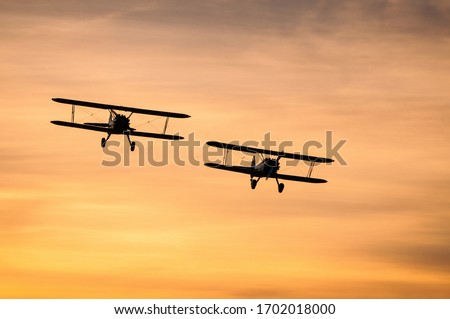 Two biplanes against an orange sunset