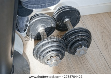 Two black adjustable dumbbells resting on a light wooden floor with natural light highlighting their textured metal weights and handles.