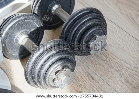 Two black adjustable dumbbells resting on a light wooden floor, ideal for weightlifting and home fitness workouts to build muscle and strength.