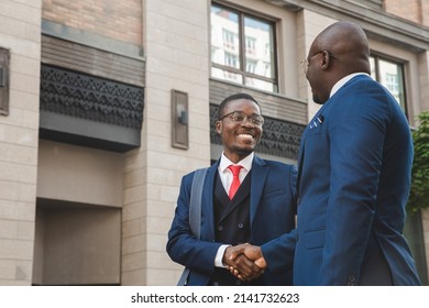 Two Black African American Businessmen In Suits And Glasses Shake Hands While Meeting Outdoors