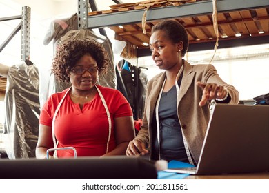 Two black African Zimbabwean ladies working in a textile factory with the supervisor helping employee with measurement using laptop computer measuring tape and steel ruler - Powered by Shutterstock