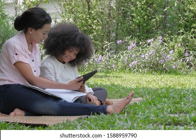 Two Black American Mother And Daughter Using Tablet For Helping Do Homework With Happy Smiling Faces At Outdoor Garden Home On Holiday. Technology With Modern Family Lifestyle Concept, Selective Focus