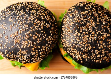 Two Black Burgers With Sesame Seed Black Bun, Beef Meat Cutlet, Cheese And Vegetables On Wooden Rustic Cutting Board Background. Close Up. Selective Soft Focus. Shallow Depth Of Field. Text Copy Space