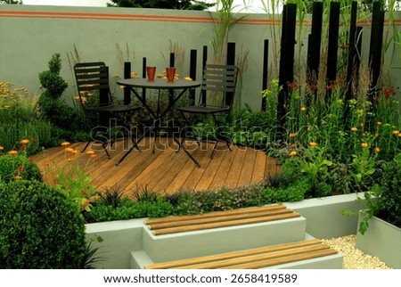 Two black chairs and a small table create a relaxing spot amidst colorful flowers and lush greenery in a landscaped garden.