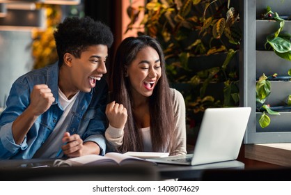 Two Black Euphoric Students Watching Exam Results On Laptop, Sitting In Cafe Or University Campus Bar, Empty Space