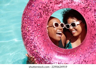 Two Black friends pose with their heads inside pink inflatable pool ring - Powered by Shutterstock