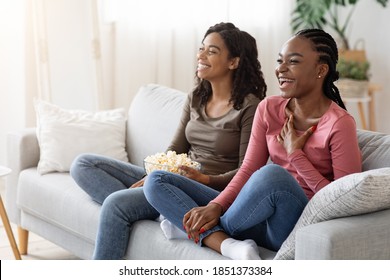 Two Black Girlfriends Having Fun At Home, Watching Comedy And Eating Popcorn, Copy Space. Laughing African American Ladies Watching Movies, Sitting On Couch At Living Room, Enjoying Weekend