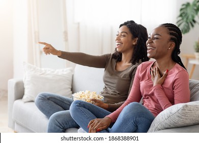 Two Black Girlfriends Having Fun At Home, Watching Comedy And Eating Popcorn, Copy Space. Laughing African American Ladies Watching Movies, Sitting On Couch At Living Room, Enjoying Weekend