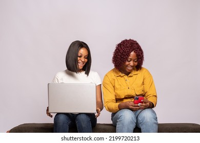 Two Black Girls Sitting Together Using Phone And Laptop