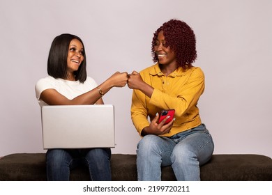 Two Black Girls Using Their Phone And Laptop Do A Fist Bump