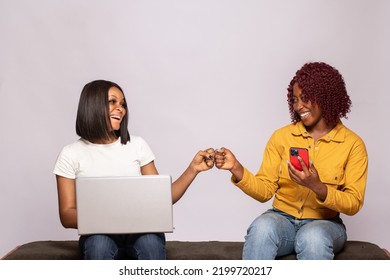 Two Black Girls Using Their Phone And Laptop Do A Fist Bump